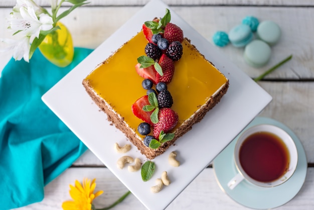 Selbst gemachter quadratischer Kuchen verziert auf gelbem Gelee und Beeren mit Minze auf hellem Hintergrund.