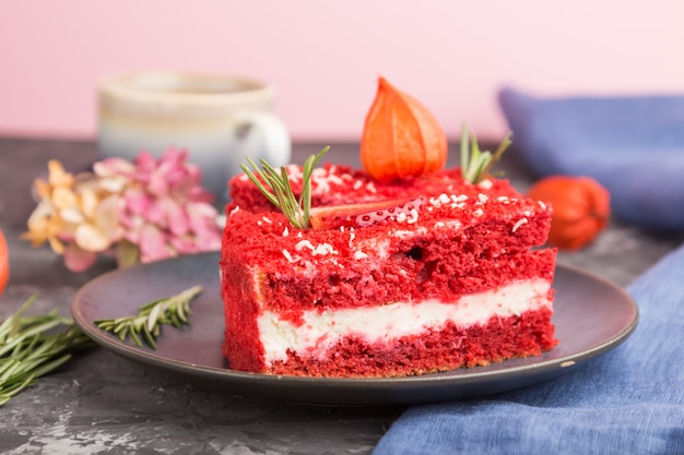 Selbst gemachter roter Samtkuchen mit Milchcreme und Erdbeere mit Tasse Kaffee auf einem schwarzen Betonhintergrund. Seitenansicht, selektiver Fokus.