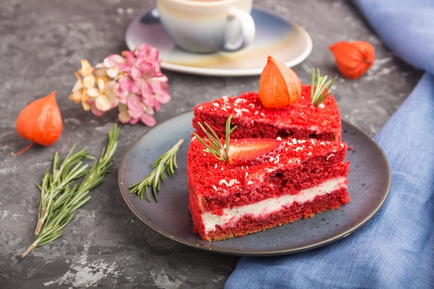 Selbst gemachter roter Samtkuchen mit Milchcreme und Erdbeere mit Tasse Kaffee auf einem schwarzen Hintergrund