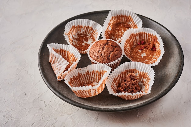 Selbst gemachter Schokoladencupcake in Backpapierform neben leeren Verpackungen auf dunklem Teller auf Holz