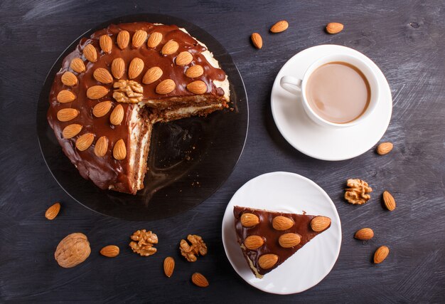 Selbst gemachter Schokoladenkuchen mit Milchcreme, Karamell und Mandeln auf schwarzem hölzernem Hintergrund.