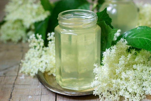 Selbst gemachter Sirup von Holunderblüten in einem Glas und Holunderzweigen auf einem Holztisch Rustikaler Stil.