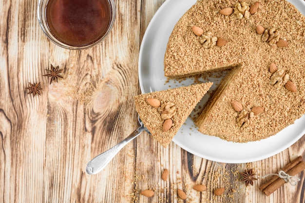 Selbst gemachter süßer geschichteter Honigkuchen mit Nüssen auf weißem Teller auf Holztisch mit Schüssel Honig, Zimt und Badian.