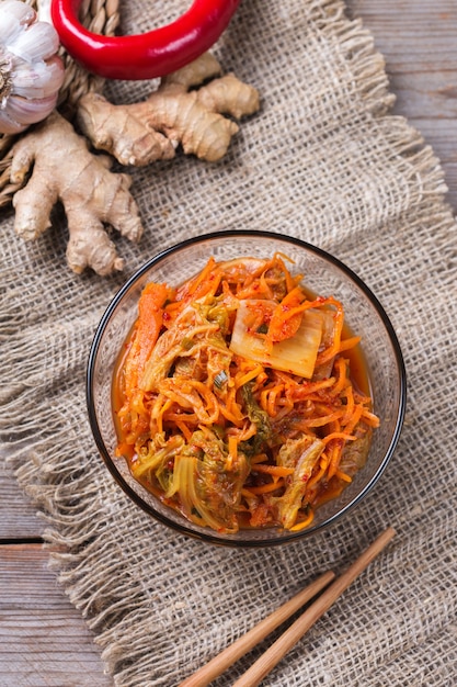 Selbst gemachter traditioneller koreanischer Kimchi-Kohlsalat aus biologischem Anbau mit Stäbchen auf einem Holztisch. Fermentiertes vegetarisches, vegan konserviertes Darmgesundheits-Lebensmittelkonzept