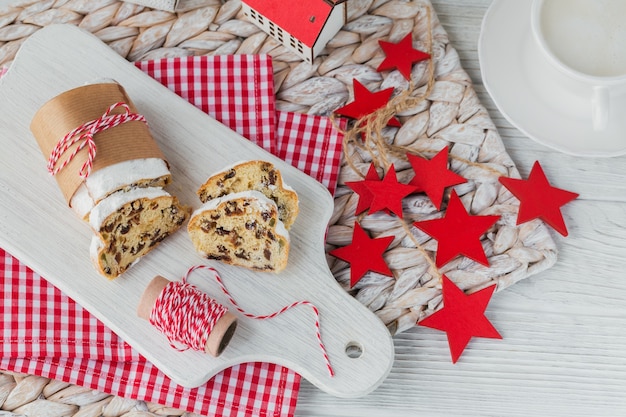 Selbst gemachter traditioneller Weihnachtsdessertstollen mit getrockneten Beeren, Nüssen und Puderzucker oben steht auf weißem rustikalem Holztisch mit Tasse Kaffee.