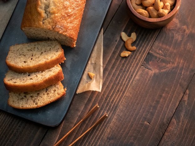 Selbst gemachtes Bananenbrotpfund geschnitten mit Acajounüssen und Honig auf Holztisch.