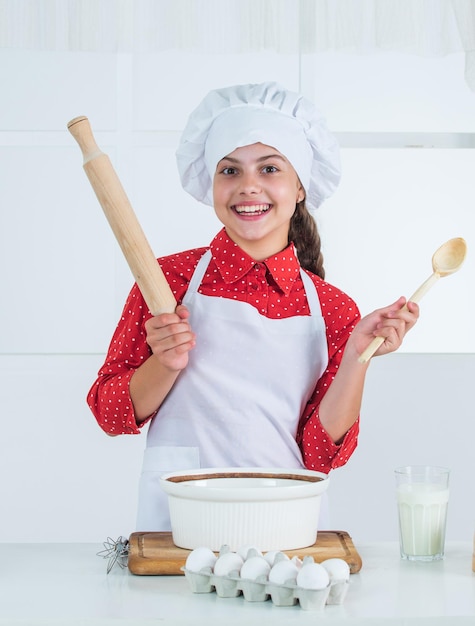 Selbst gemachtes Gebäck glückliche Kindheit glückliches jugendlich Mädchen, das Teigkind in der Kochuniform kocht