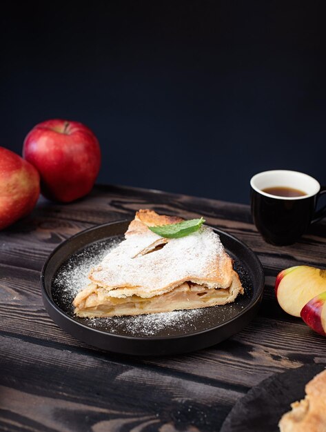 Selbst gemachtes Stück Apfelkuchen mit frischen roten Äpfeln auf schwarzem Tisch