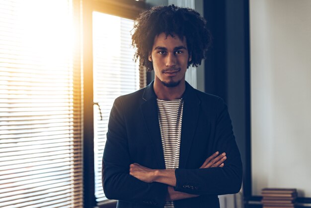 Foto selbstbewusst. junger gutaussehender afrikanischer mann, der die arme verschränkt hält und in die kamera schaut