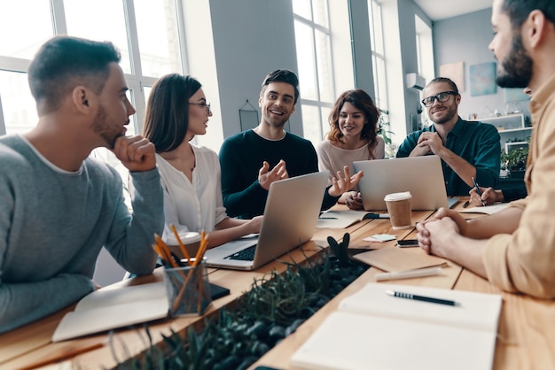 Foto selbstbewusst und klug. gruppe junger moderner menschen in eleganter freizeitkleidung, die etwas diskutieren und lächeln, während sie im kreativbüro arbeiten working