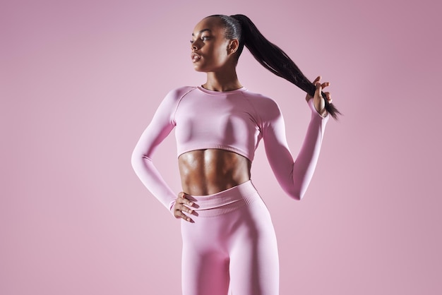 Selbstbewusste afrikanische Frau in Sportkleidung, die ihre Haare gegen einen rosa Hintergrund anpasst
