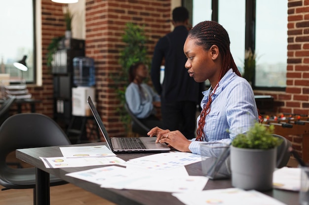 Selbstbewusste afroamerikanische Geschäftsfrau, die Projektfinanzstatistiken analysiert. Unternehmensleiter, der im modernen Büro an Managementplan und Marketingstrategie arbeitet.