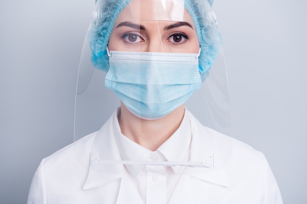 selbstbewusste Arztdame trägt einen medizinischen Schutzmaskenschild isoliert auf grauer Wand