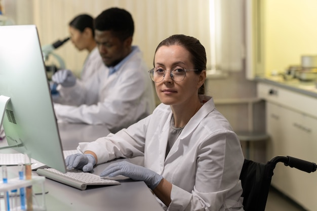 Selbstbewusste Chemikerin mit Computer am Arbeitsplatz gegen zwei Kollegen