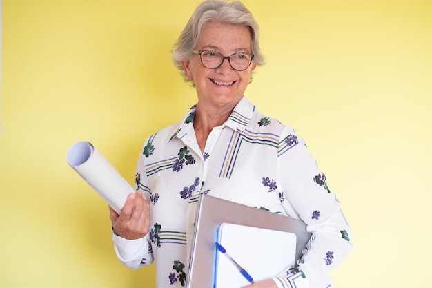 Selbstbewusste, erfahrene Architech-Seniorin mit Laptop und Notizbuch in der Hand isoliert auf gelbem Hintergrund