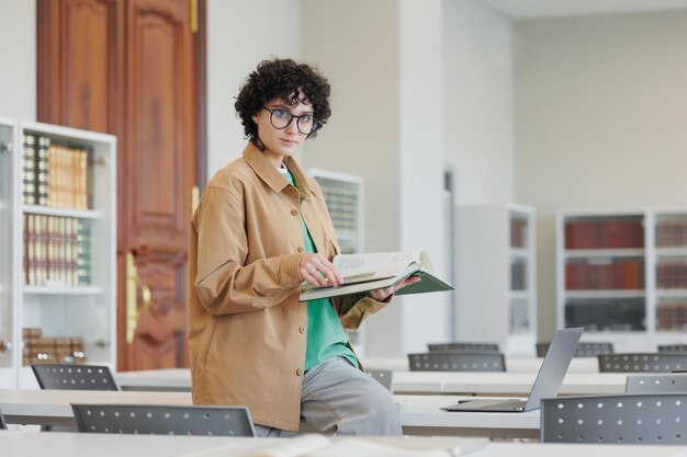 Selbstbewusste Frau in Bibliothek oder Coworking arbeitet Laptop-Online-Studentin liest Buch