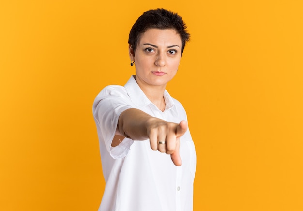 selbstbewusste Frau mittleren Alters, die auf orangefarbene Wand isoliert nach vorne schaut und zeigt