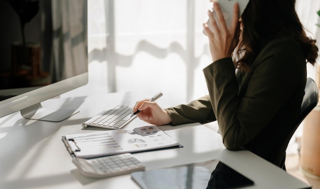 Selbstbewusste Geschäftsexpertin, attraktive lächelnde junge Frau, die Laptop tippt und ein digitales Tablet auf dem Schreibtisch im kreativen Heimbüro hält