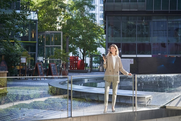 Selbstbewusste Geschäftsfrau im beigen Anzug, die in Machtpose im Stadtzentrum steht