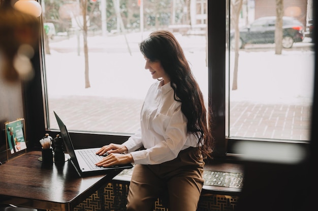 Selbstbewusste junge Frau in einem Business-Anzug arbeitet an einem Laptop, während sie am Fenster in einem Café sitztGeschäftsfrau