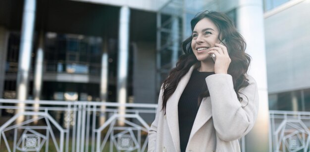 Selbstbewusste junge Geschäftsfrau, die am Handy mit einem breiten Lächeln auf ihrem Gesicht außerhalb spricht