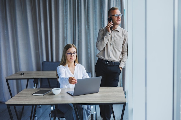 Selbstbewusste männliche und weibliche kollegen in eleganter freizeitkleidung besprechen ein projekt am arbeitsplatz und genießen firmenfreundschaften. glückliche partner unterhalten sich auf einem mobiltelefon über büronetzwerke