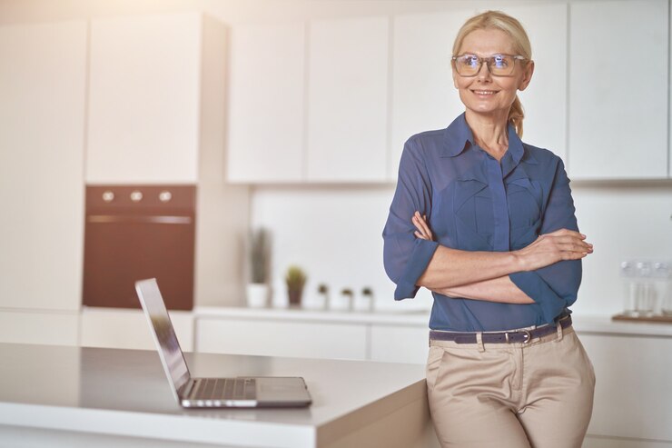 Foto selbstbewusste reife geschäftsfrau mit brille, die bei der arbeit zu hause mit dem laptop lächelt, der mit steht