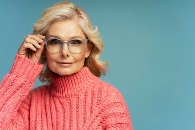 Selbstbewusste, reife Geschäftsfrau mit Brille, die isoliert auf blauem Hintergrund in die Kamera blickt