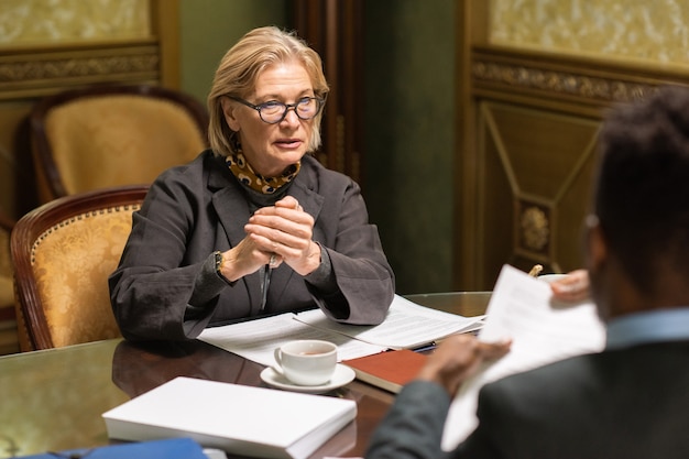 Selbstbewusste reife Geschäftsfrau mit Brille, die Kollegen anschaut