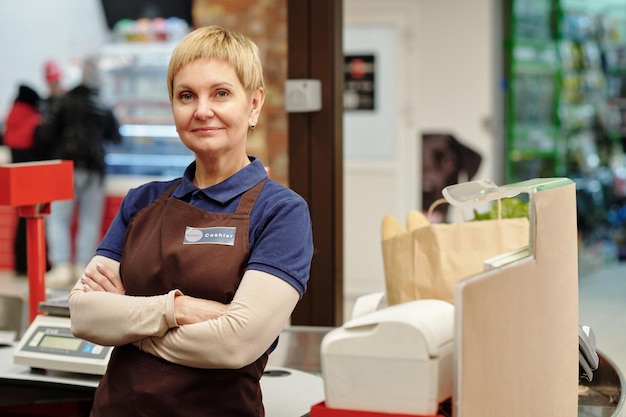 Selbstbewusste, reife Verkäuferin in Uniform, die in die Kamera blickt