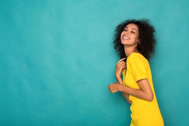 Selbstbewusste Schönheit. Fröhliches afroamerikanisches Mädchen in gelber Kleidung posiert im Studio auf blauem Hintergrund, Kopierraum