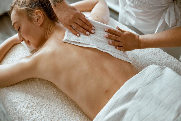 Selbstbewusste Spezialistin macht entspannende Körpermassage für schöne schlanke kaukasische Dame im minimalistischen Spa-Salon