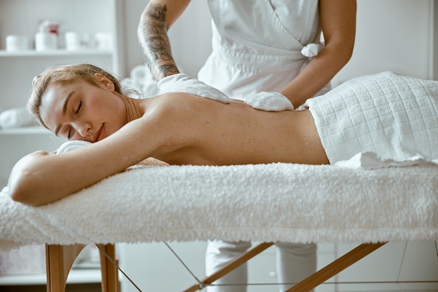 Selbstbewusste Spezialistin macht entspannende Körpermassage für schöne schlanke kaukasische Dame im minimalistischen Spa-Salon