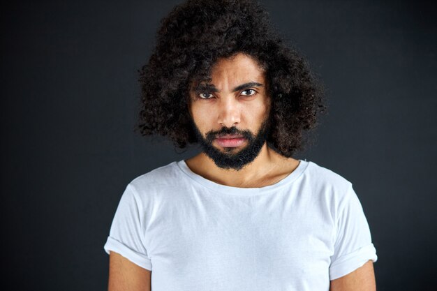 Selbstbewusster arabischer Mann im weißen T-Shirt mit tiefem Blick, Blick auf Kamera, lockiger Kerl ist ernst