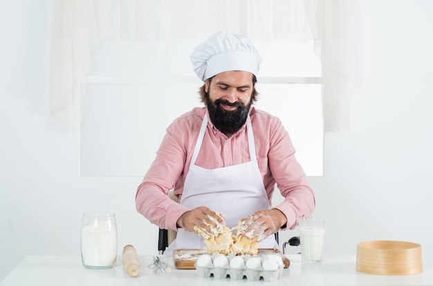 Selbstbewusster bärtiger Mann mit Kochmütze, männlicher Koch, der Essen in der heimischen Küche zubereitet