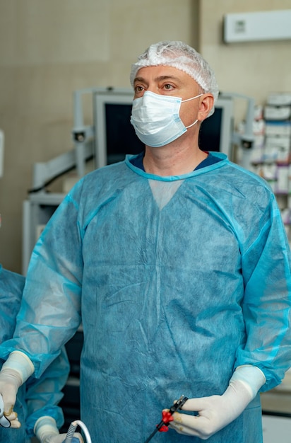 Foto selbstbewusster chirurg, der eine schutzmaske trägt, die spezielle ausrüstung hält und während der operation am konzept der patientenmedizin arbeitet