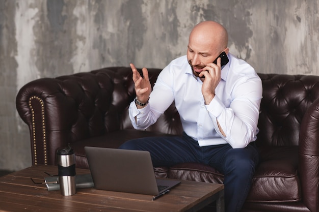 Selbstbewusster erwachsener Mann spricht am Telefon, das am Computer sitzt