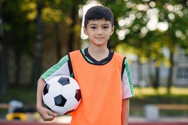 Selbstbewusster Fußballspieler in orangefarbener Weste hält einen Ball