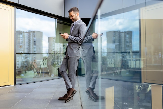 Foto selbstbewusster geschäftsmann lächelt in einem scharfen anzug vor einer modernen bürofassade aus glas