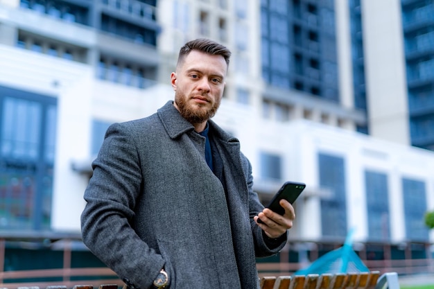 Selbstbewusster Geschäftsmann mit Telefon in der modernen Stadtstraße Stilvoller gutaussehender Mann, der in der neuen Straßenstadt steht