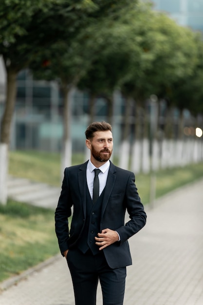 Selbstbewusster Geschäftsmann. Selbstbewusster junger Mann im vollen Anzug, der seinen Ärmel anpasst und weg schaut, während er draußen mit Stadtbild im Hintergrund steht