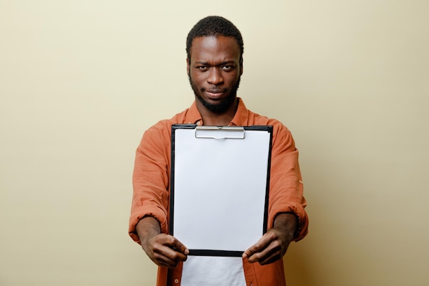 Selbstbewusster junger Afroamerikaner, der die Zwischenablage in die Kamera isoliert auf weißem Hintergrund hält
