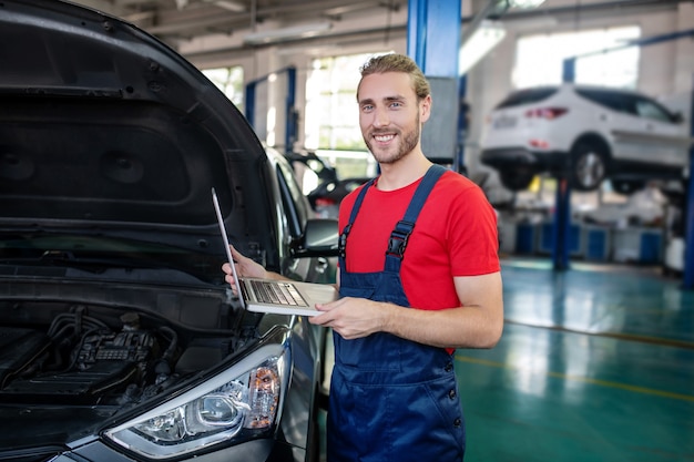 Selbstbewusster junger erwachsener Mann in der Arbeitsuniform, die an Autos arbeitet