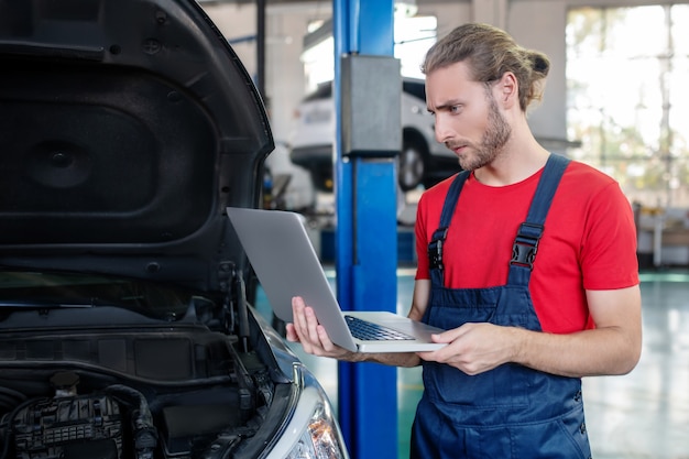 Selbstbewusster junger erwachsener Mann in der Arbeitsuniform, die an Autos arbeitet