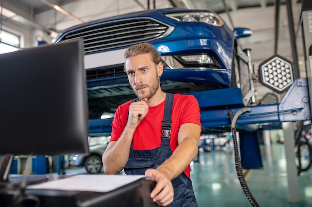 Selbstbewusster junger erwachsener Mann in der Arbeitsuniform, die an Autos arbeitet