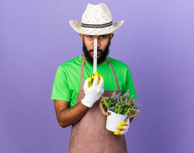 Selbstbewusster junger Gärtner, der eine Blume im Blumentopf mit Maßband hält