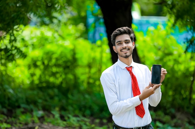 Selbstbewusster junger Inder, der sein Smartphone zeigt