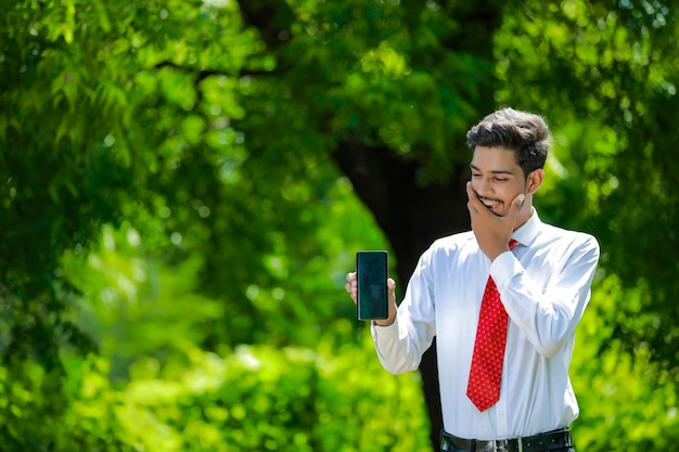 Selbstbewusster junger Inder, der sein Smartphone zeigt