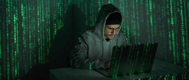 Selbstbewusster junger Mann im Kapuzenhemd mit Computer vor dunklem Hintergrund