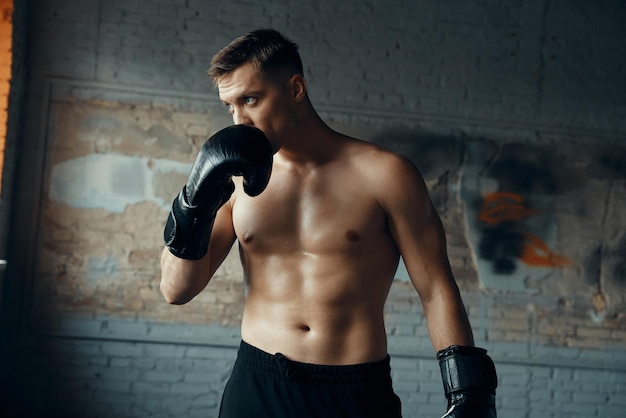 Selbstbewusster junger Mann in Boxhandschuhen berührt das Gesicht und blickt weg, während er im Fitnessstudio steht